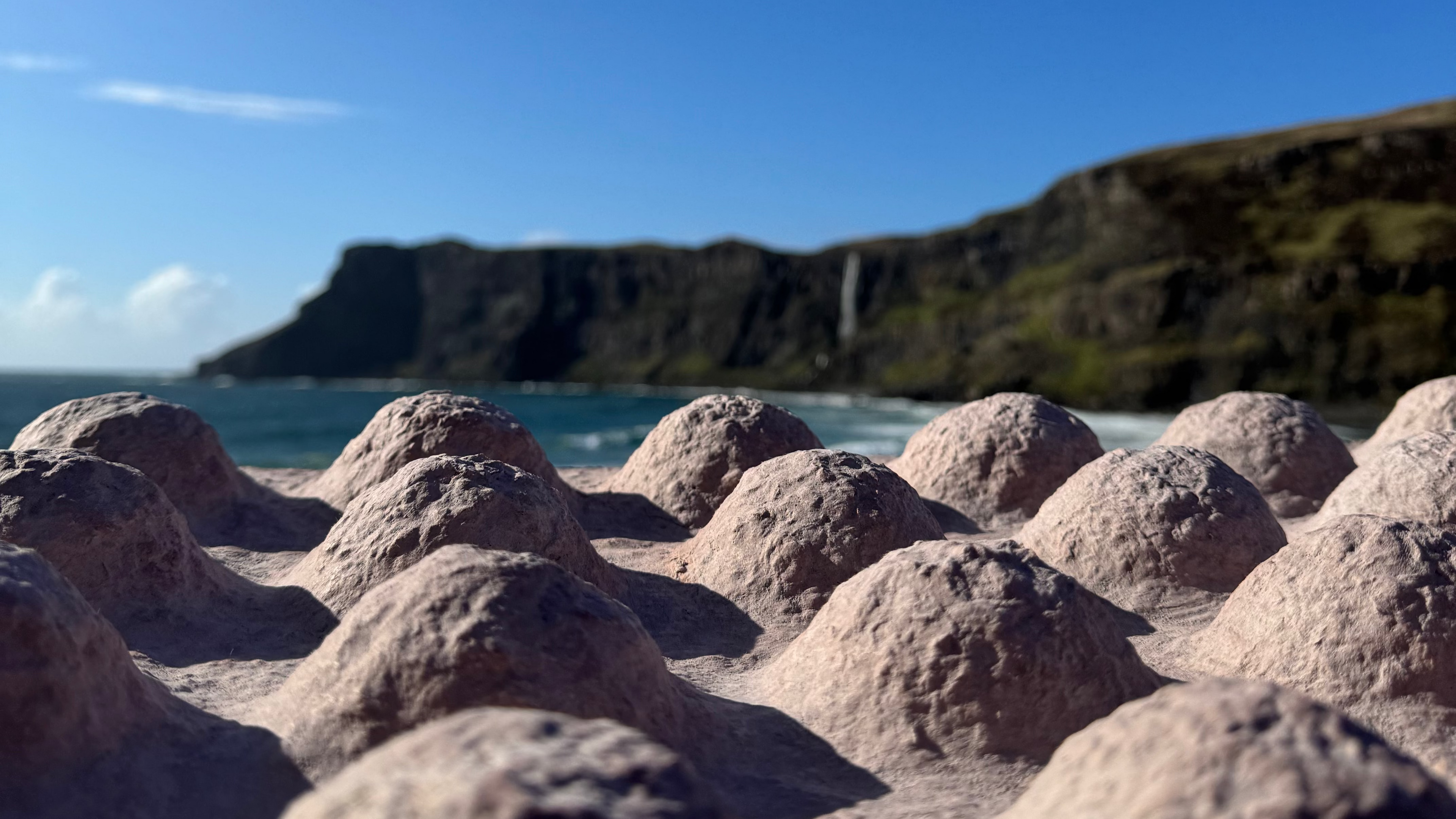 Close-up of a bio-mineral wall panel at surface level, its sculpted relief echoing the sea cliffs and coastline behind it in Scotland