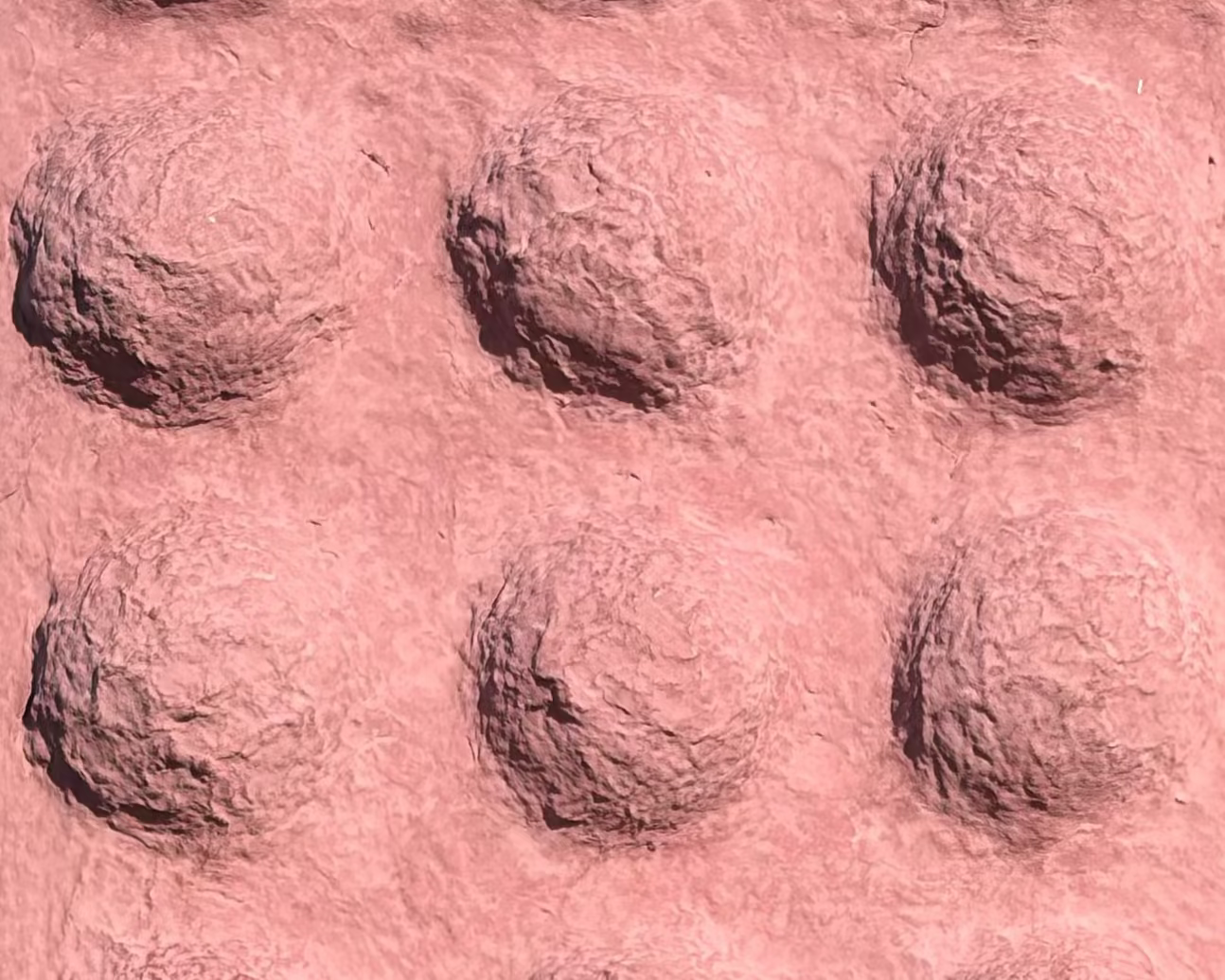 A rectangular pink textured panel with raised circular bumps, photographed outdoors on grass beside rocks with hills and blue sky in the background.