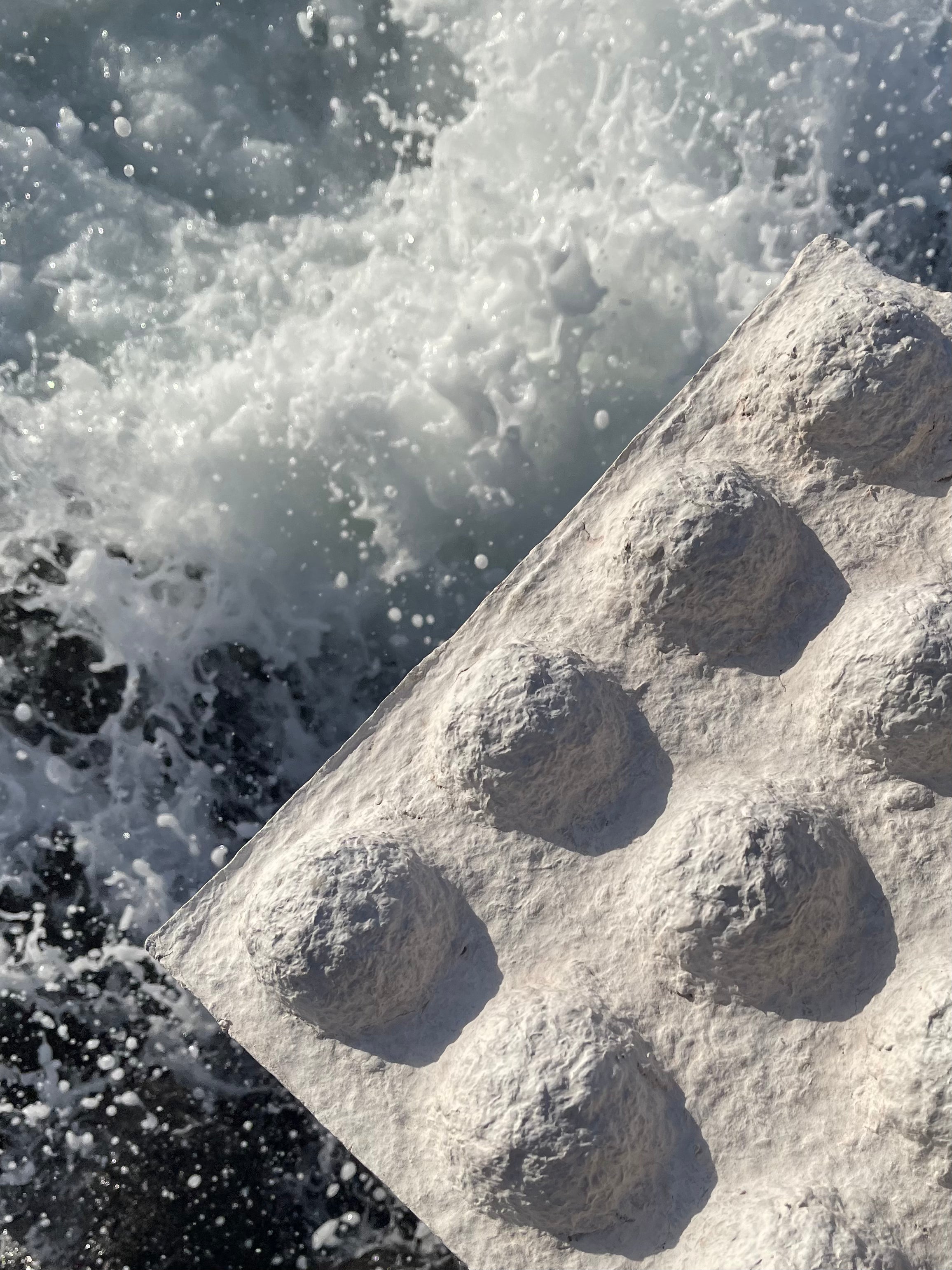 Hand-sculpted bio-mineral wall panel against sea foam, close-up of the mineral surface texture